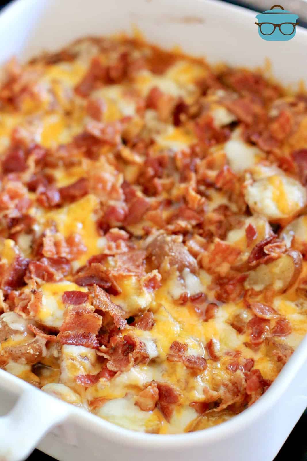 melted cheese and crumbled bacon shown on cooked potatoes in a white baking dish.