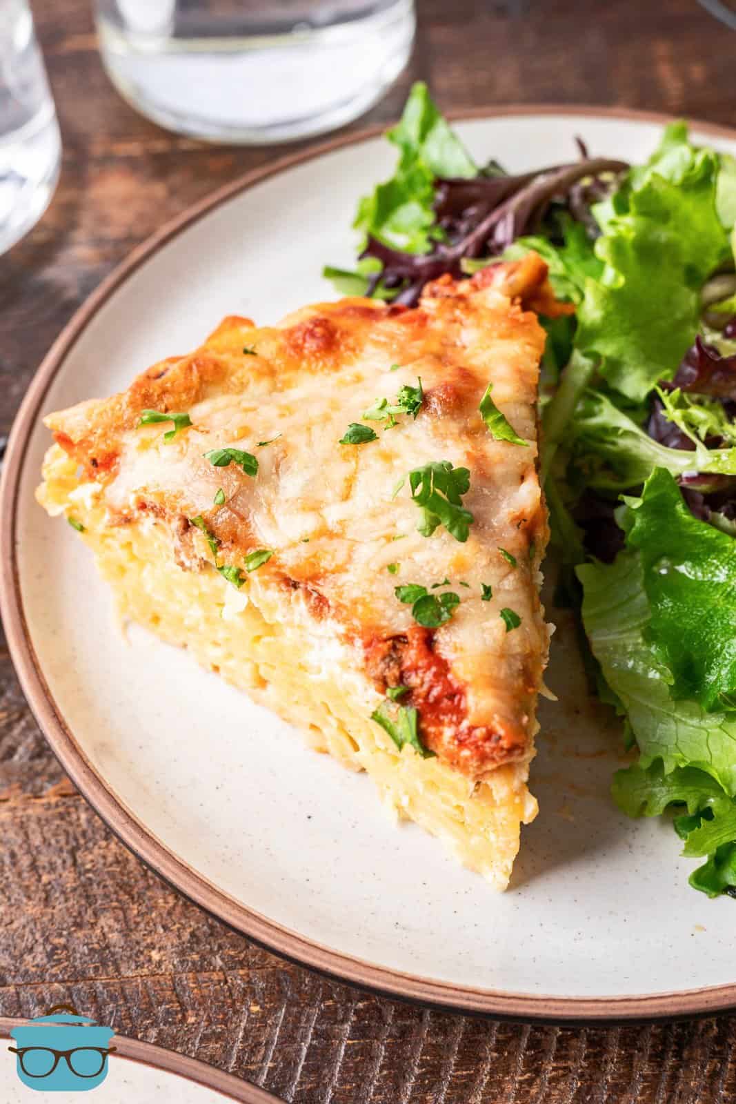 a slice of spaghetti pie on a plate with a green side salad. 