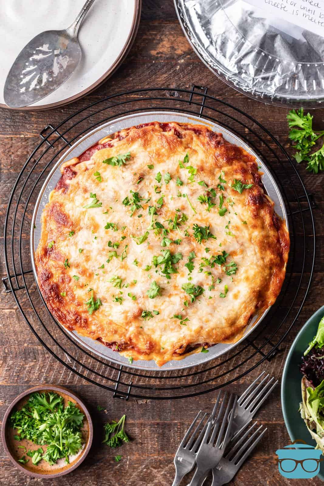 overhead photo of fully baked spaghetti pie on a round cooling rack on a wood surface. 