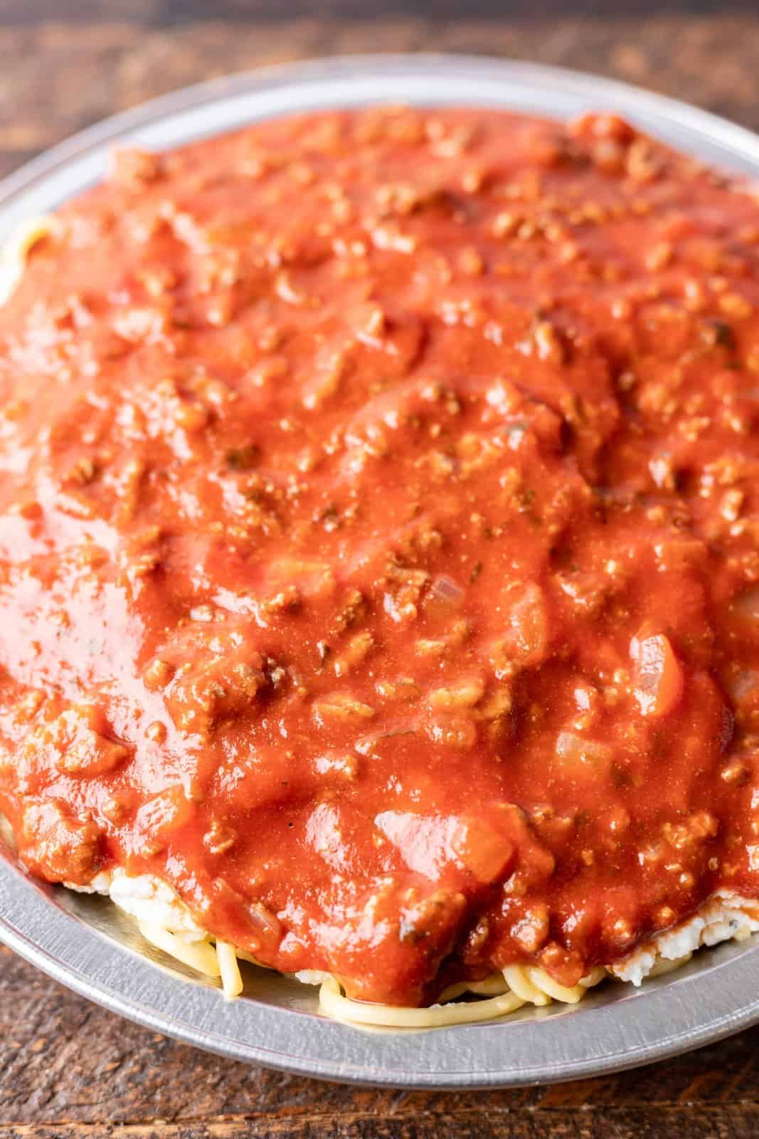 beef spaghetti sauce spread on top of cooked spaghetti noodles in pie pan. 