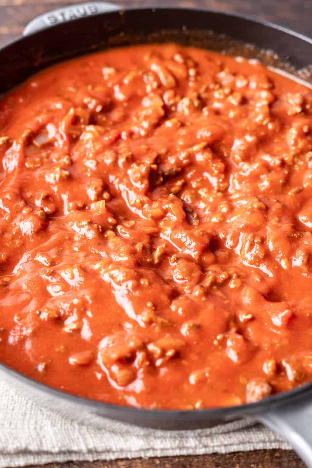 marinara sauce stirred together with ground beef in a skillet. 