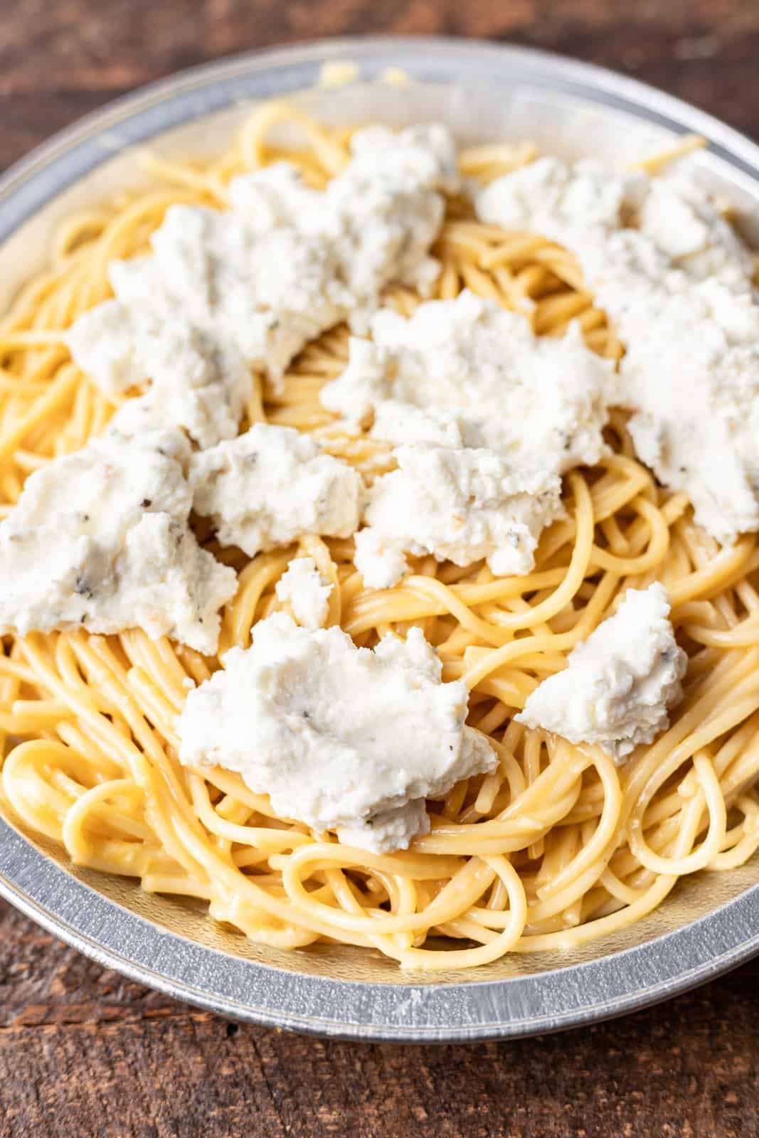 dollops of ricotta cheese on top of spaghetti in a disposable pan. 