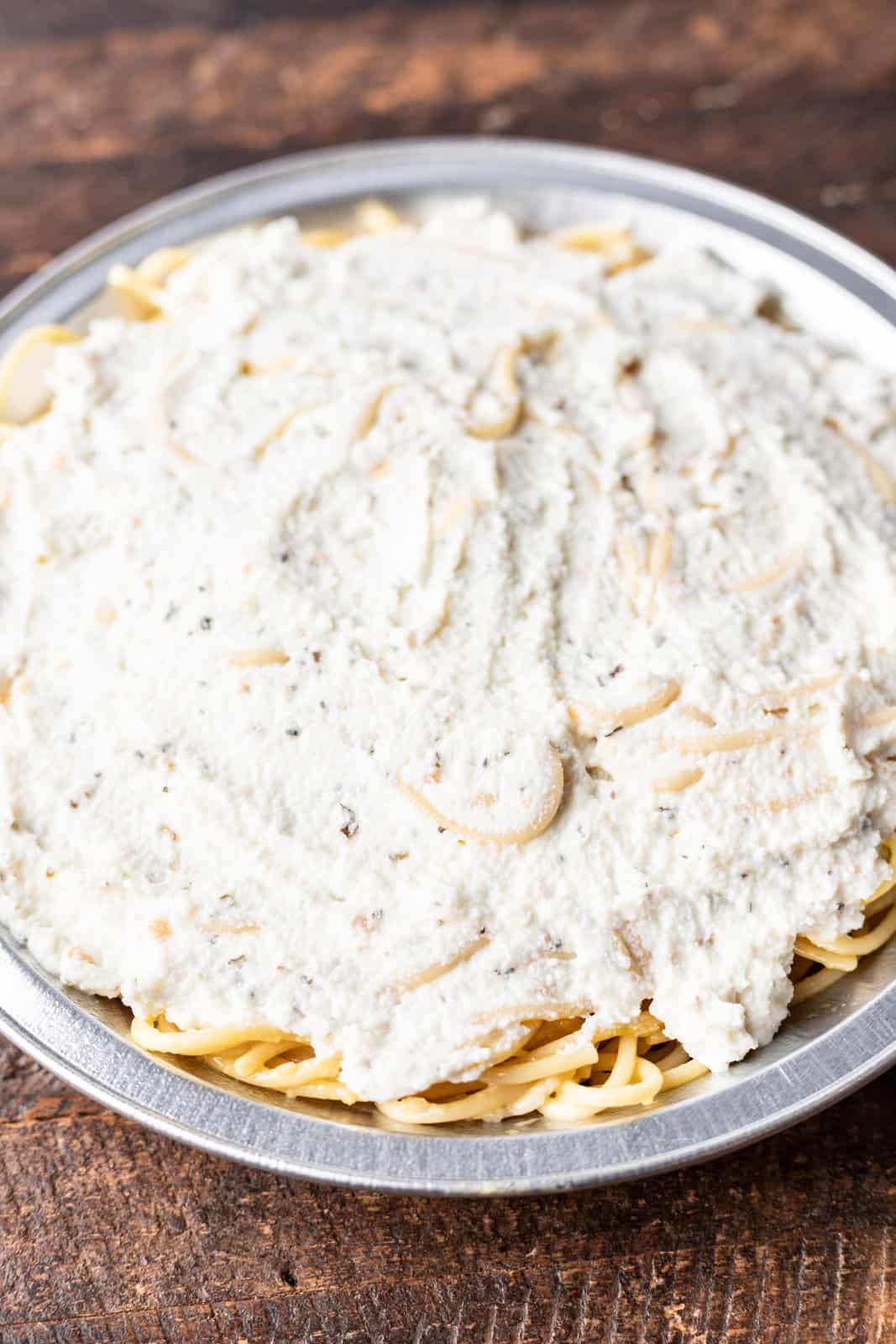 ricotta cheese spread over baked spaghetti noodles in a pan.