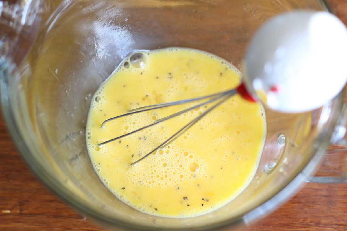 eggs being whisked together and seasoned with salt and pepper in a measuring cup.