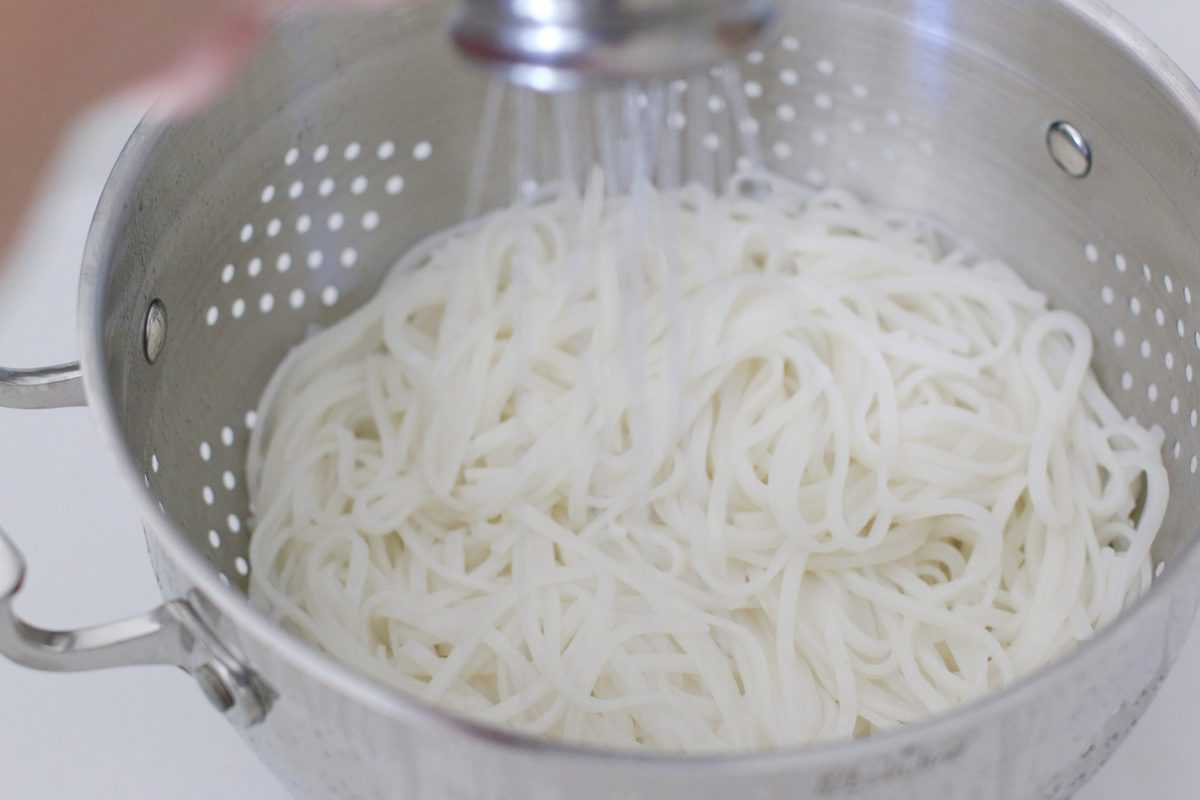 draining rice noodles in a silver colander.