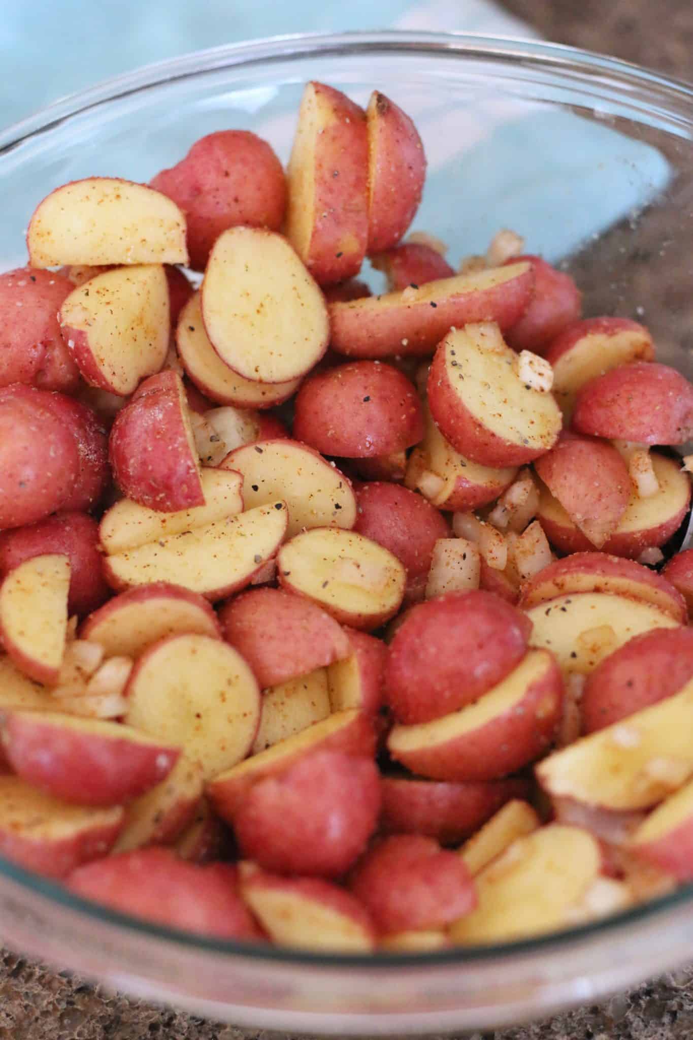 sliced red potatoes with seasoning stirred together in a bowl.