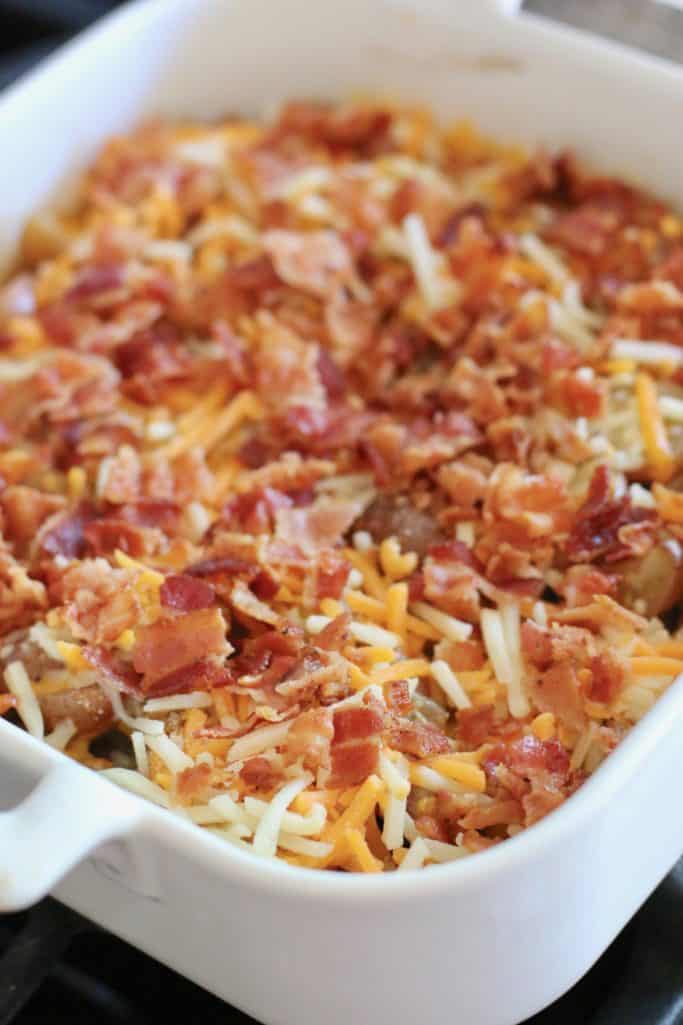 baked baby potatoes topped with shredded cheddar cheese and cooked and crumbled bacon in a square 8x8 white Revol baking dish