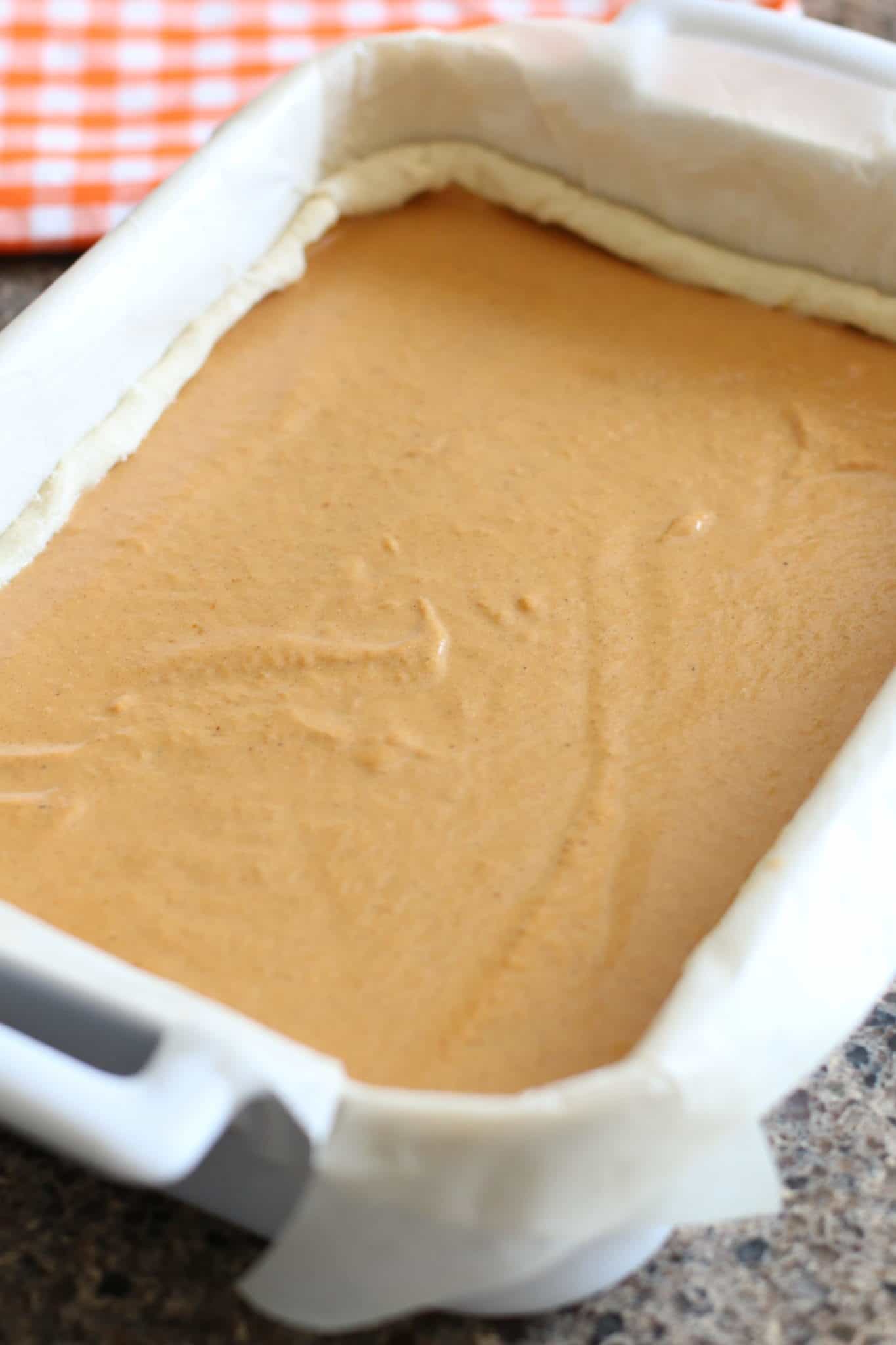Pumpkin Pie Filling spread into crescent roll dough on top of parchment paper in a Rovel white baking dish.