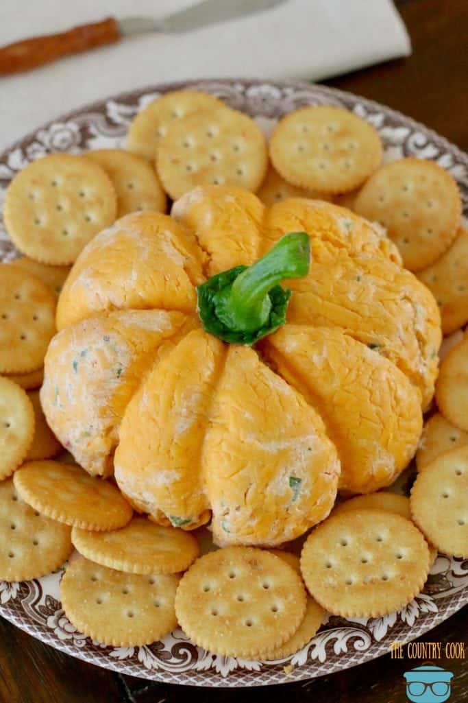 Pumpkin Shaped Cheese Ball with cheddar cheese and ranch dressing shown on a plate with Ritz crackers.