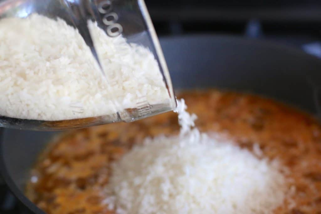 pouring Minute Rice into large skillet with ground beef and taco seasoning mixture.
