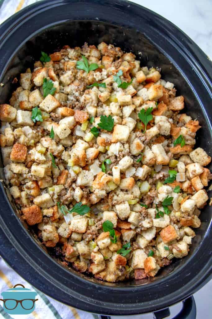 The Best Crock Pot Stuffing (Dressing) showing in a black oval crock pot and sprinkled with chopped parsley.