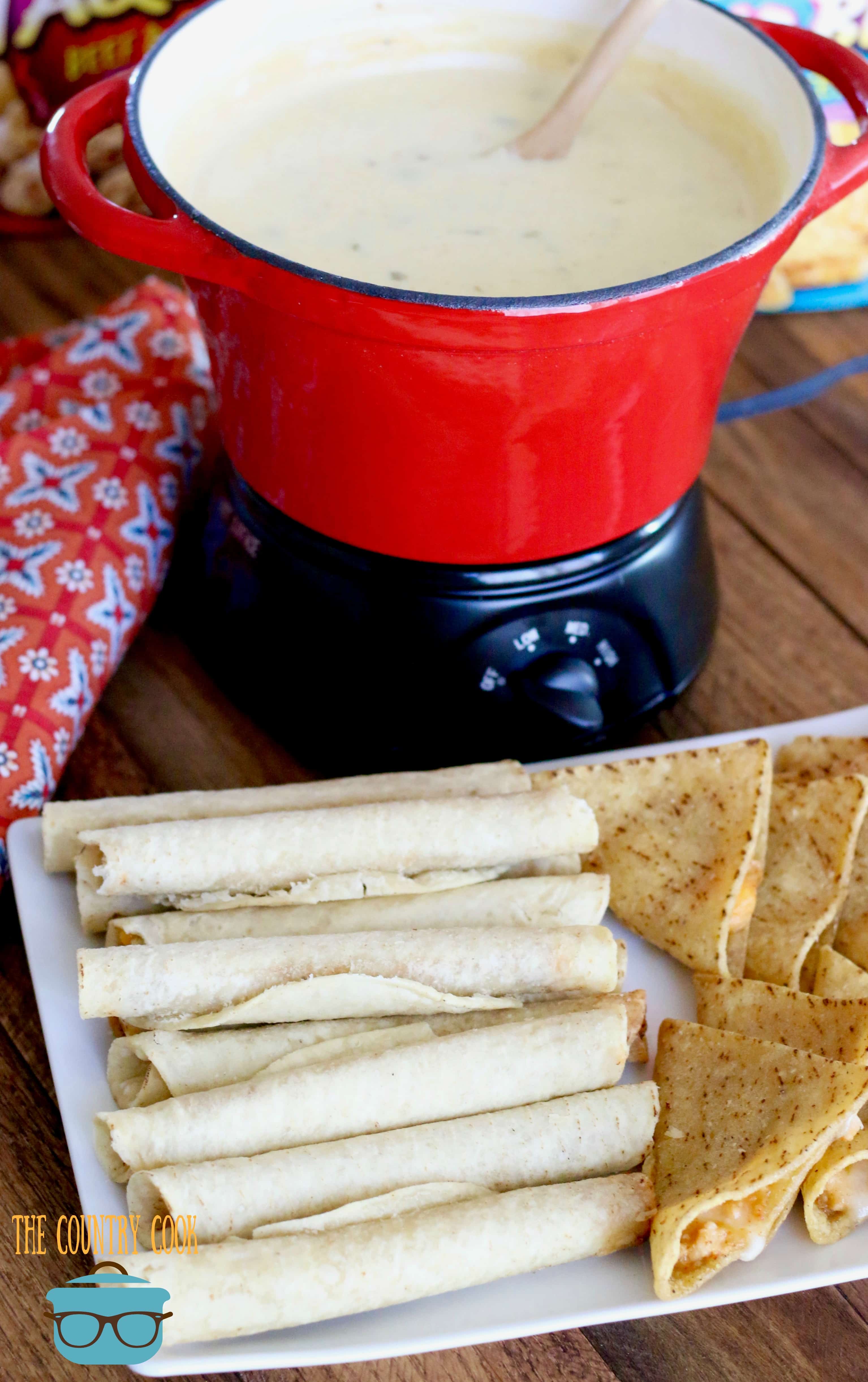 Crock Pot Queso Blanco Dip shown in the background with a tray of taquitos and mini tacos on a platter towards the front. 