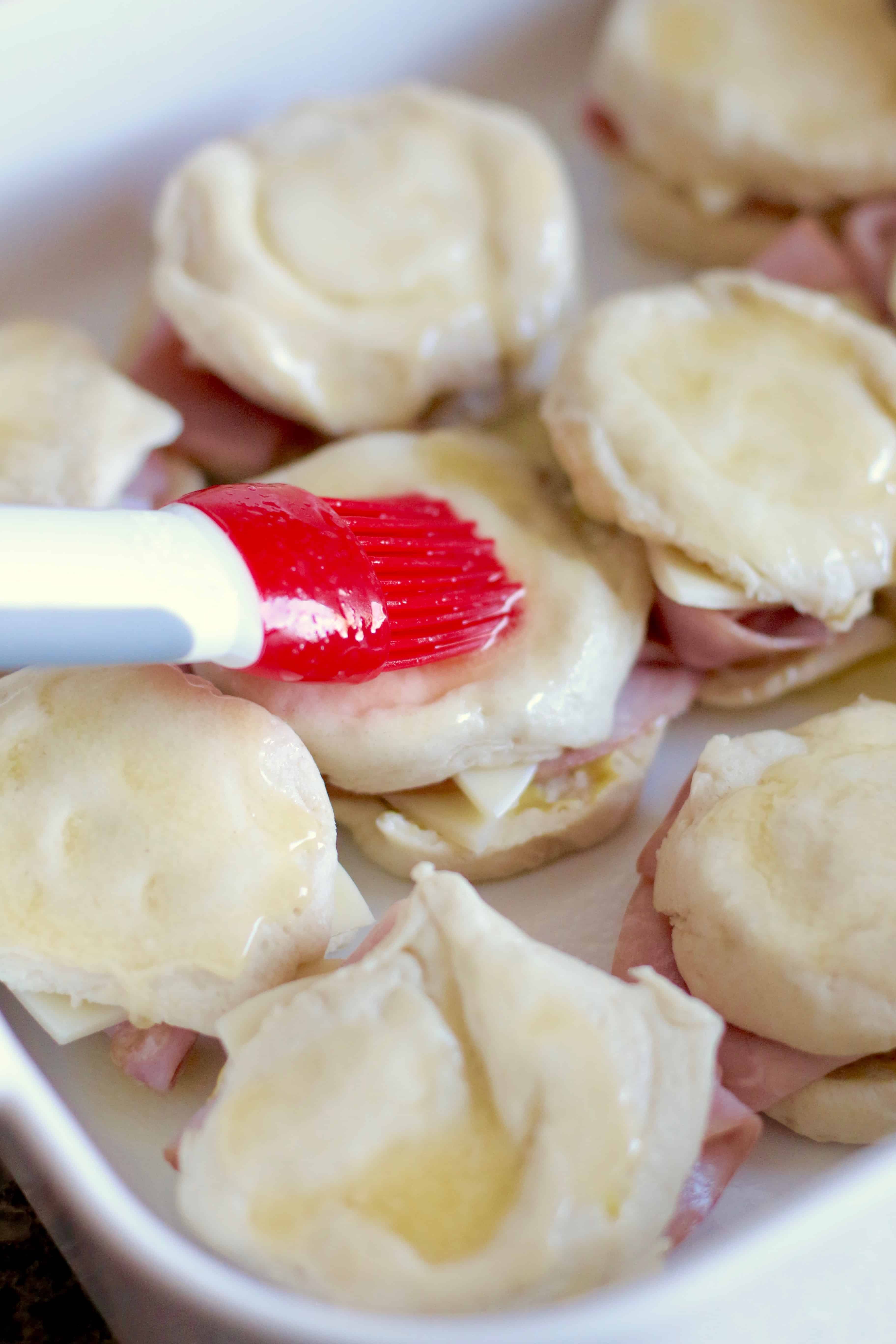 brushing butter on top of ham biscuits.
