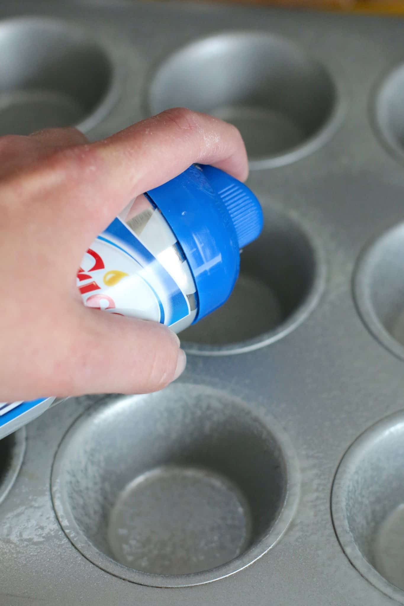 hand shown spraying nonstick cooking spray in a muffin pan.