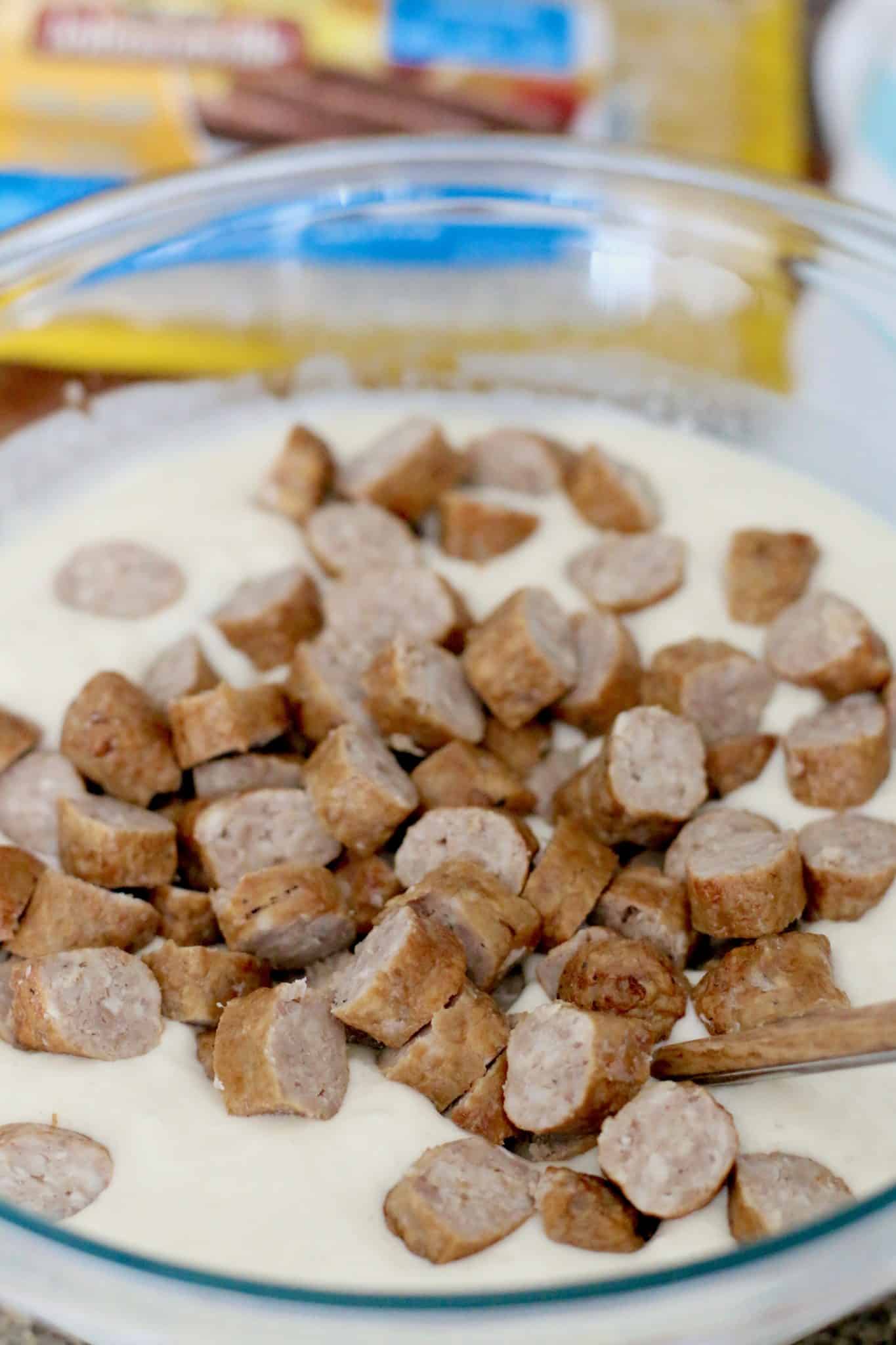 sliced cooked breakfast sausages on top of prepared pancake batter mix in a bowl.