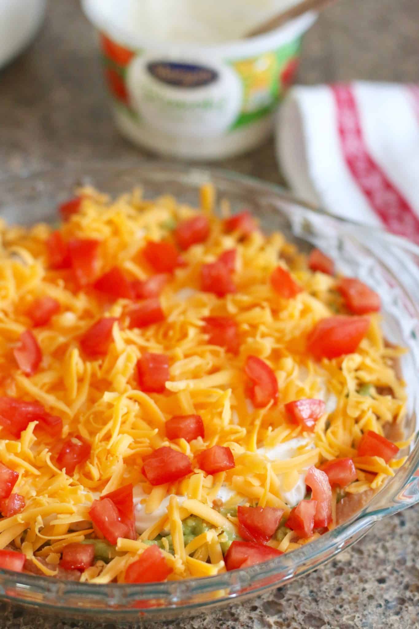 mexican layer dip topped with shredded cheese and diced tomatoes