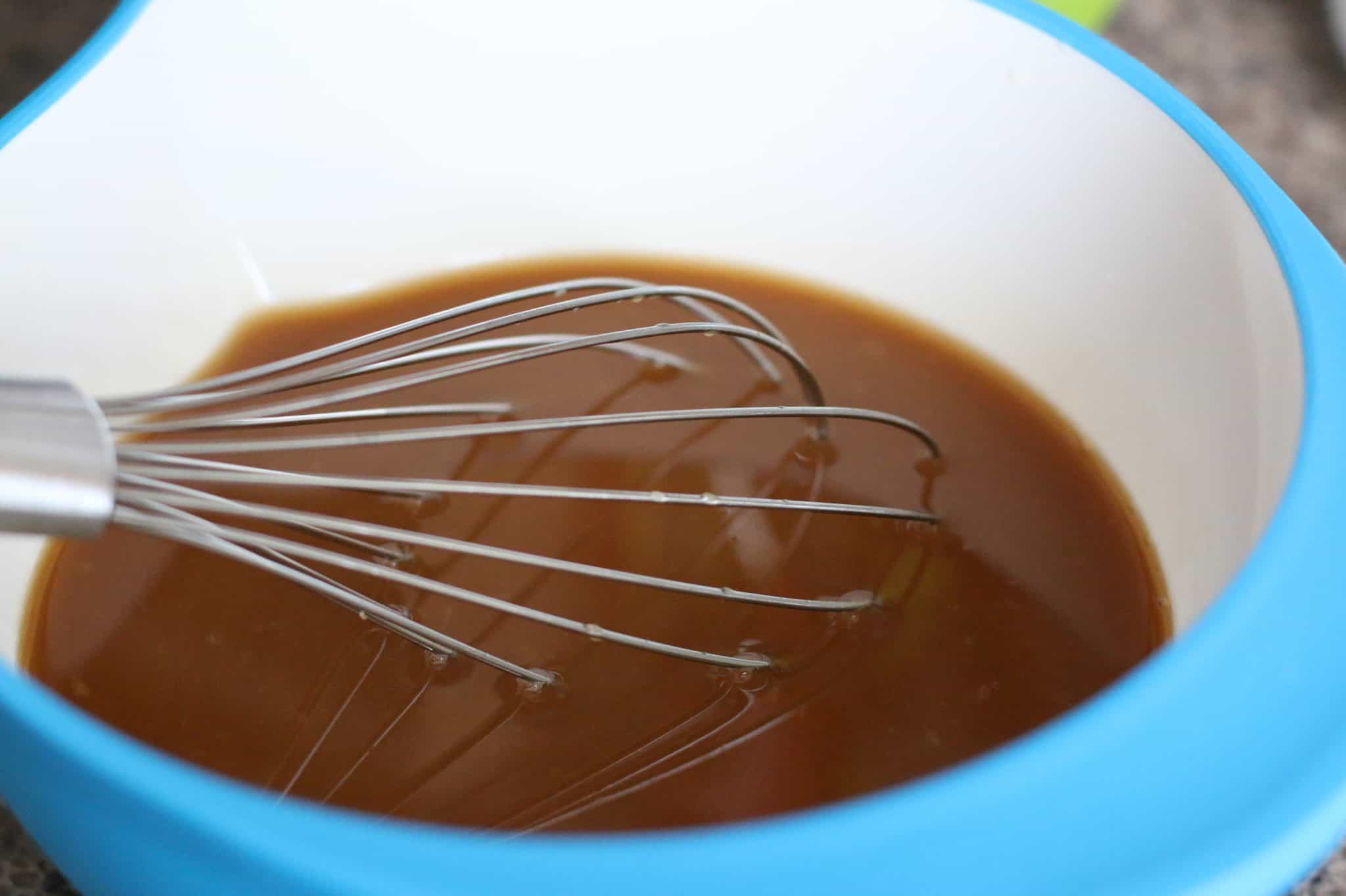 sweet and sour glaze being mixed with a whisk in a blue and white bowl. 