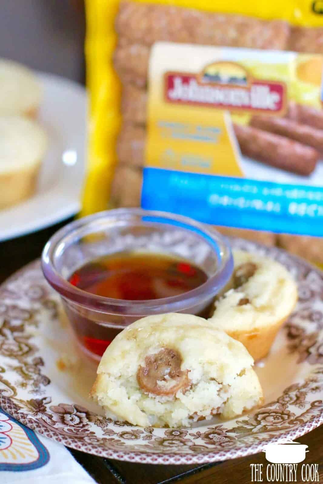 two pancake sausage muffins shown on a plate with a small bowl of maple syrup on the side. 