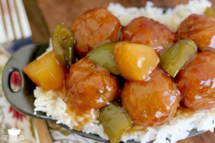 Crock Pot Sweet and Sour Meatballs shown on a bed of rice in a small black cast iron dish.