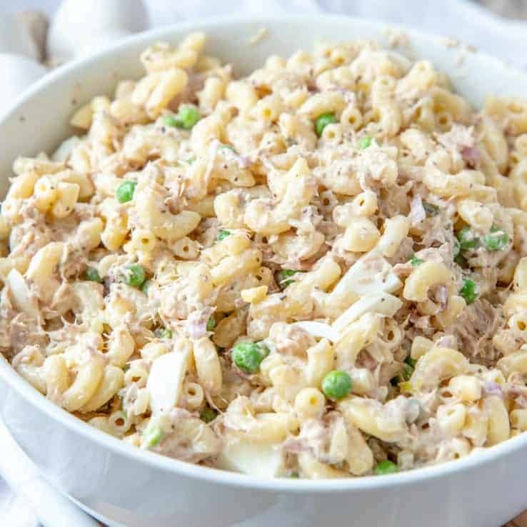 a close up photo of tuna macaroni salad shown in a large white serving bowl.
