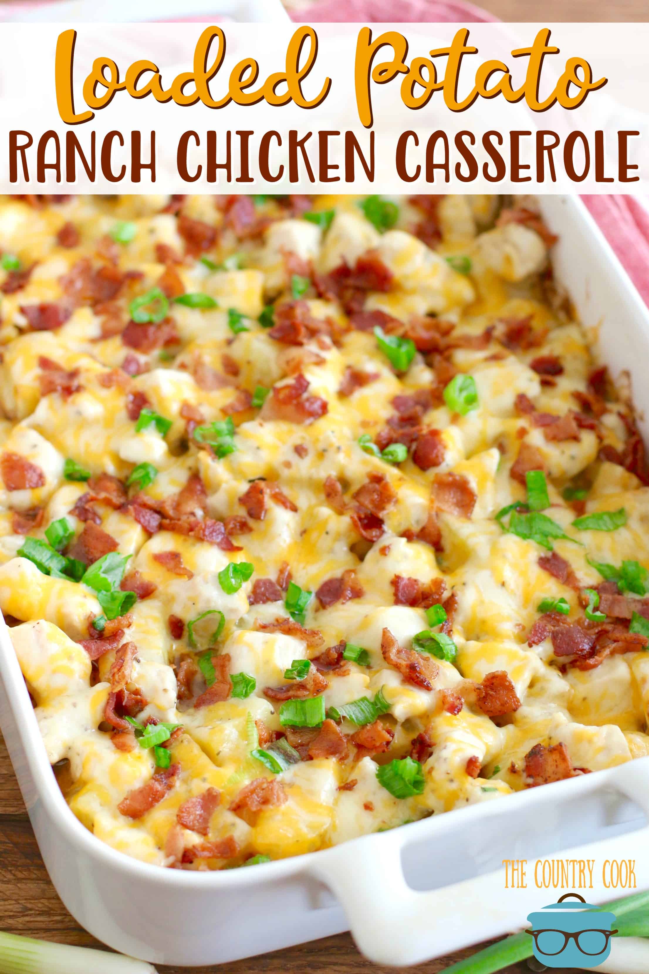 Loaded Potato Ranch Chicken Casserole recipe from The Country Cook. Cheese, potatoes and chicken in a white baking dish topped with melted cheese, sliced cooked bacon and sliced green onions.