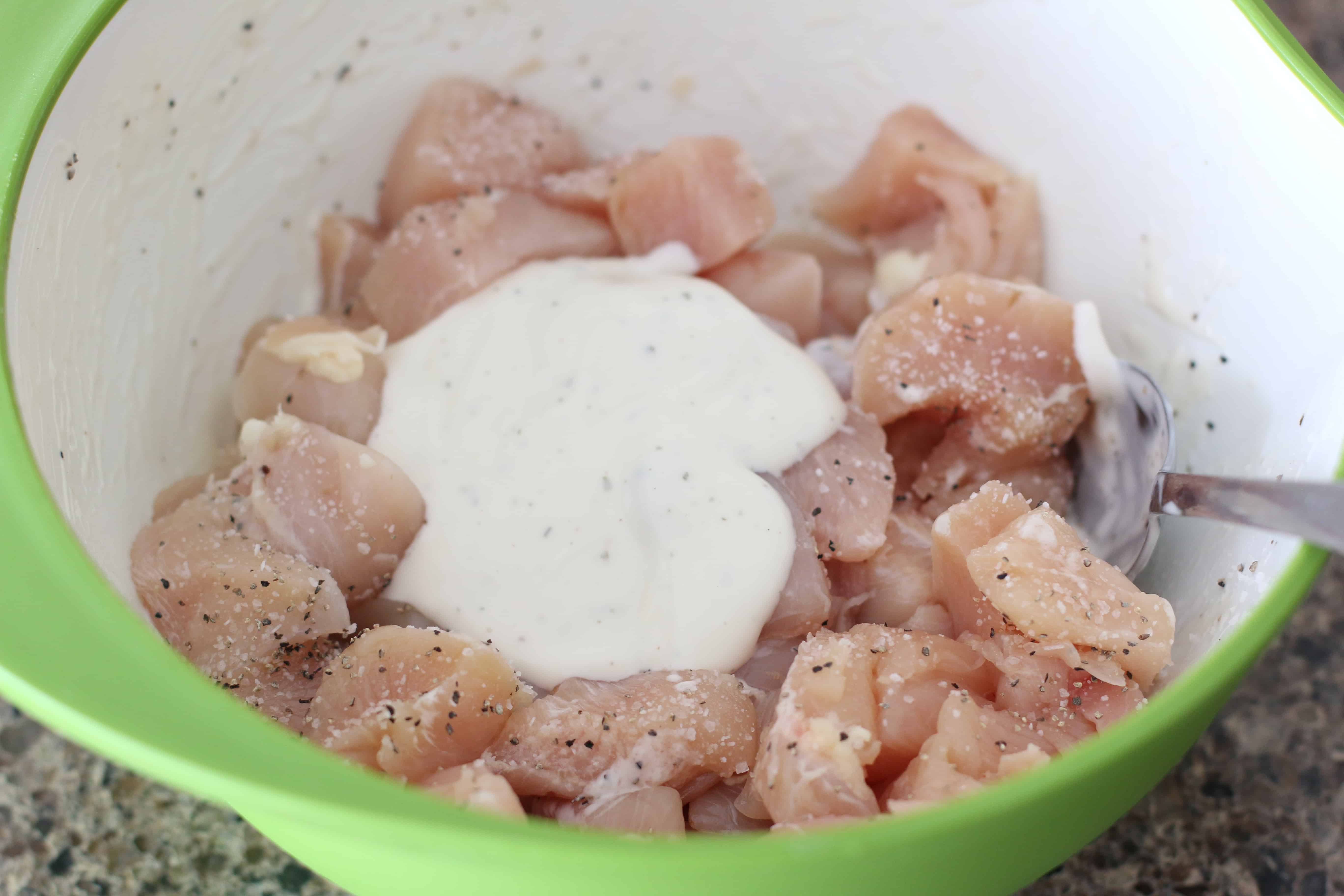 diced chicken breasts, ranch dressing, salt and pepper in a bowl with a spoon.
