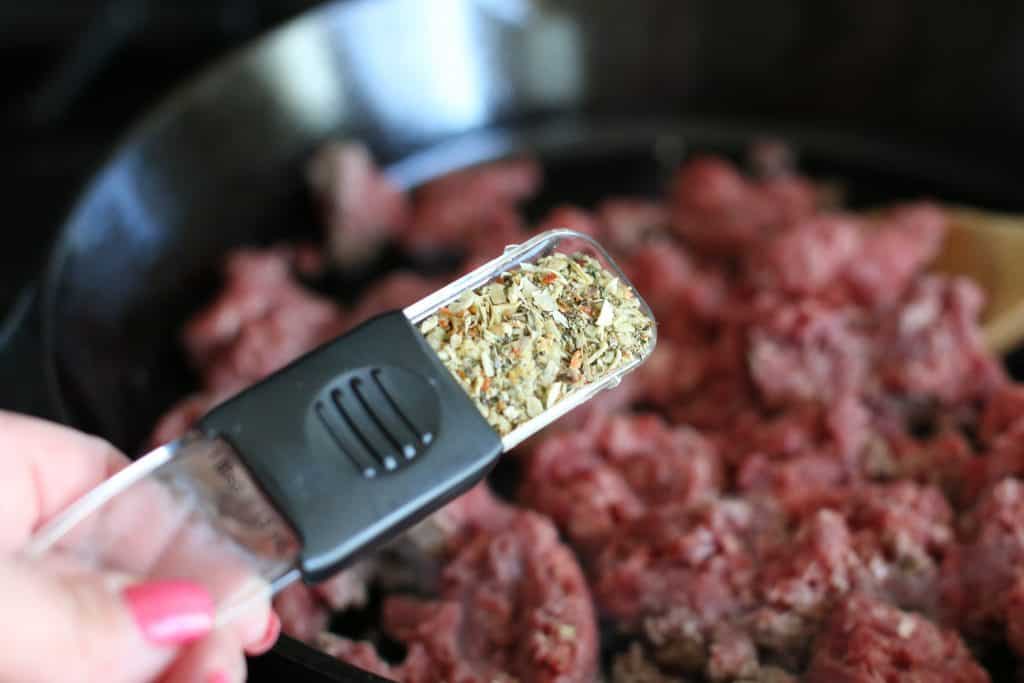 Italian seasoning added to the ground beef in a skillet.