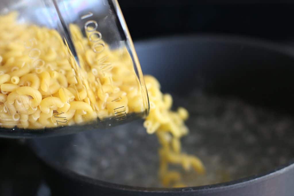 elbow macaroni noodles being poured into boiling water. 