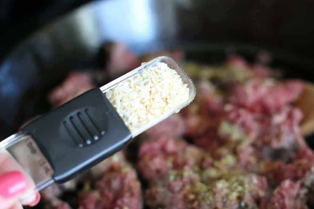 onion flakes being added to cooking ground beef.