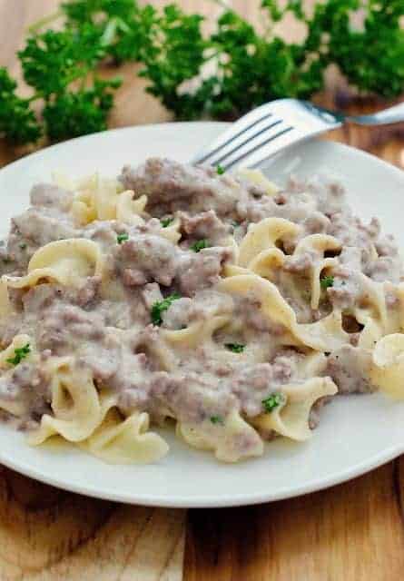 beef stroganoff served over egg noodles on a round white plate with fresh parsley in the background