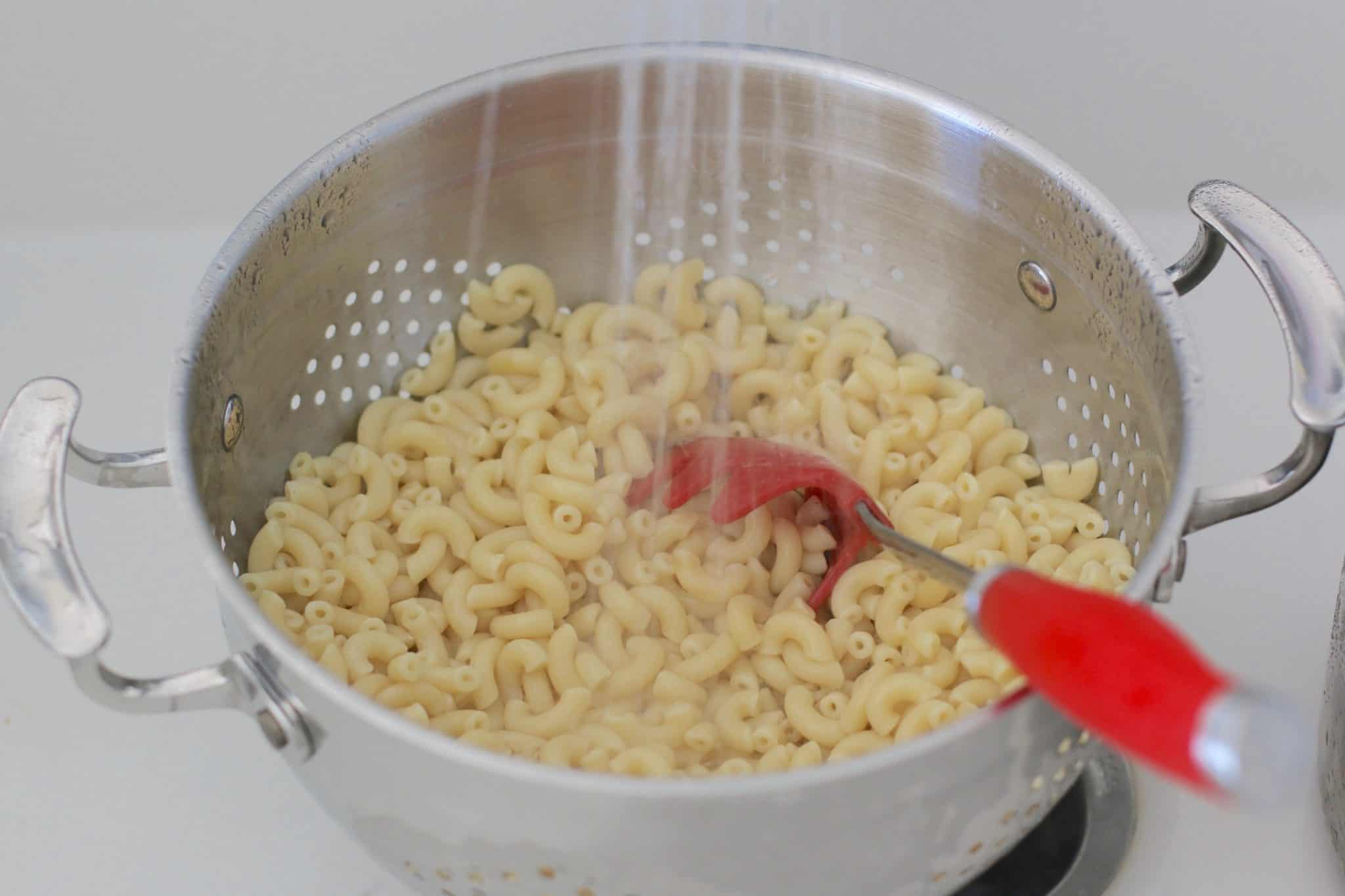 rinsing macaroni noodles in a large colander.