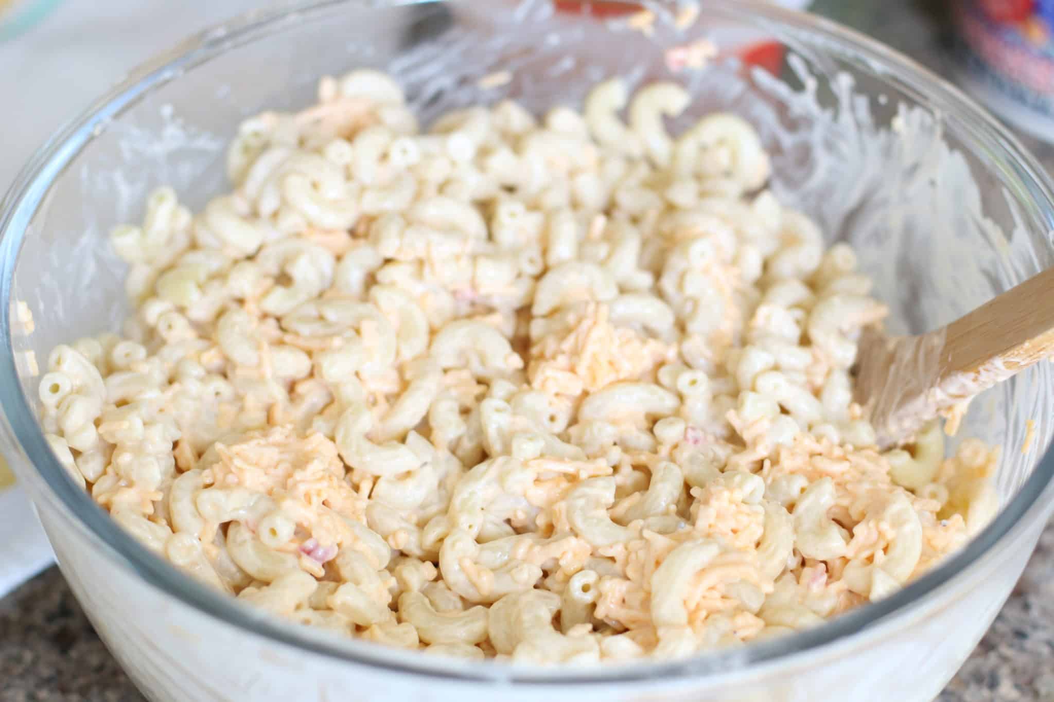 macaroni salad with pimiento cheese and mayonnaise mixture in a large clear bowl.