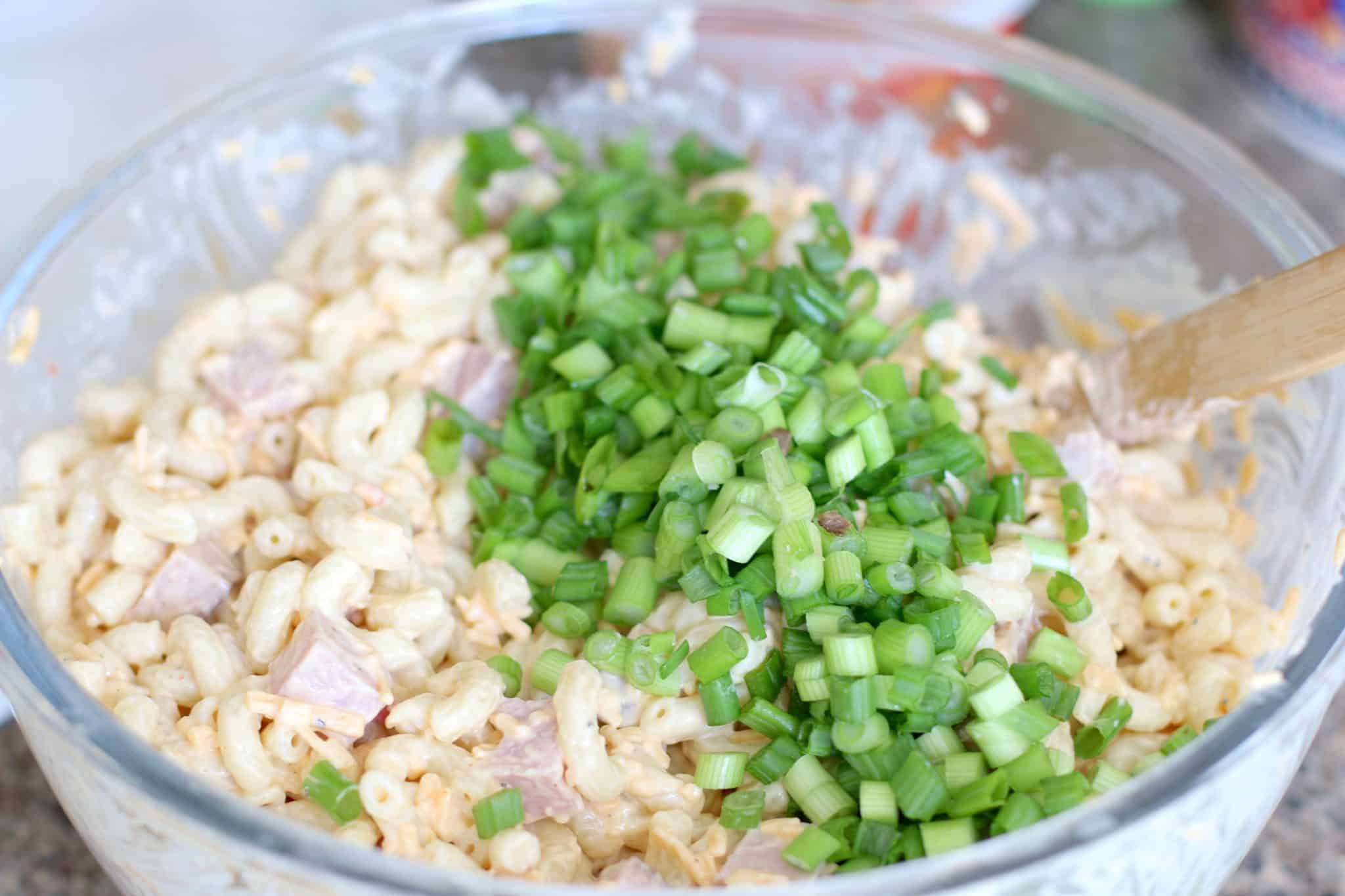 green onion, ham, macaroni salad with mayonnaise, salt and pepper in a large bowl stirred with a wooden spoon.