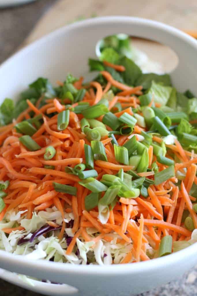 romaine lettuce, cole slaw, sliced carrots, sliced green onions in a large white bowl.