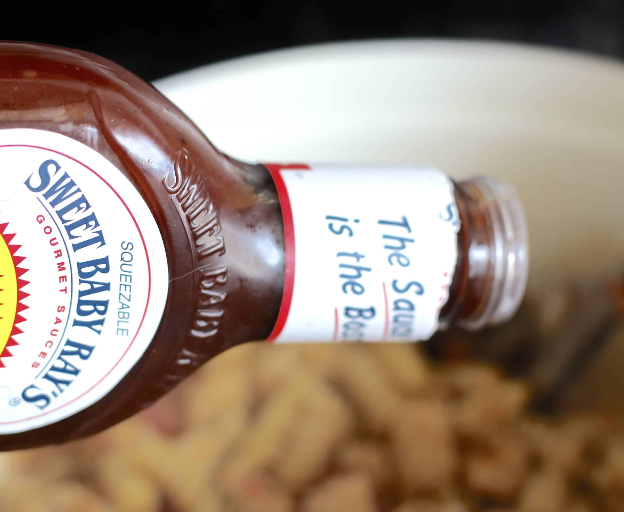 pouring Sweet Baby Ray's BBQ sauce into pasta mixture.