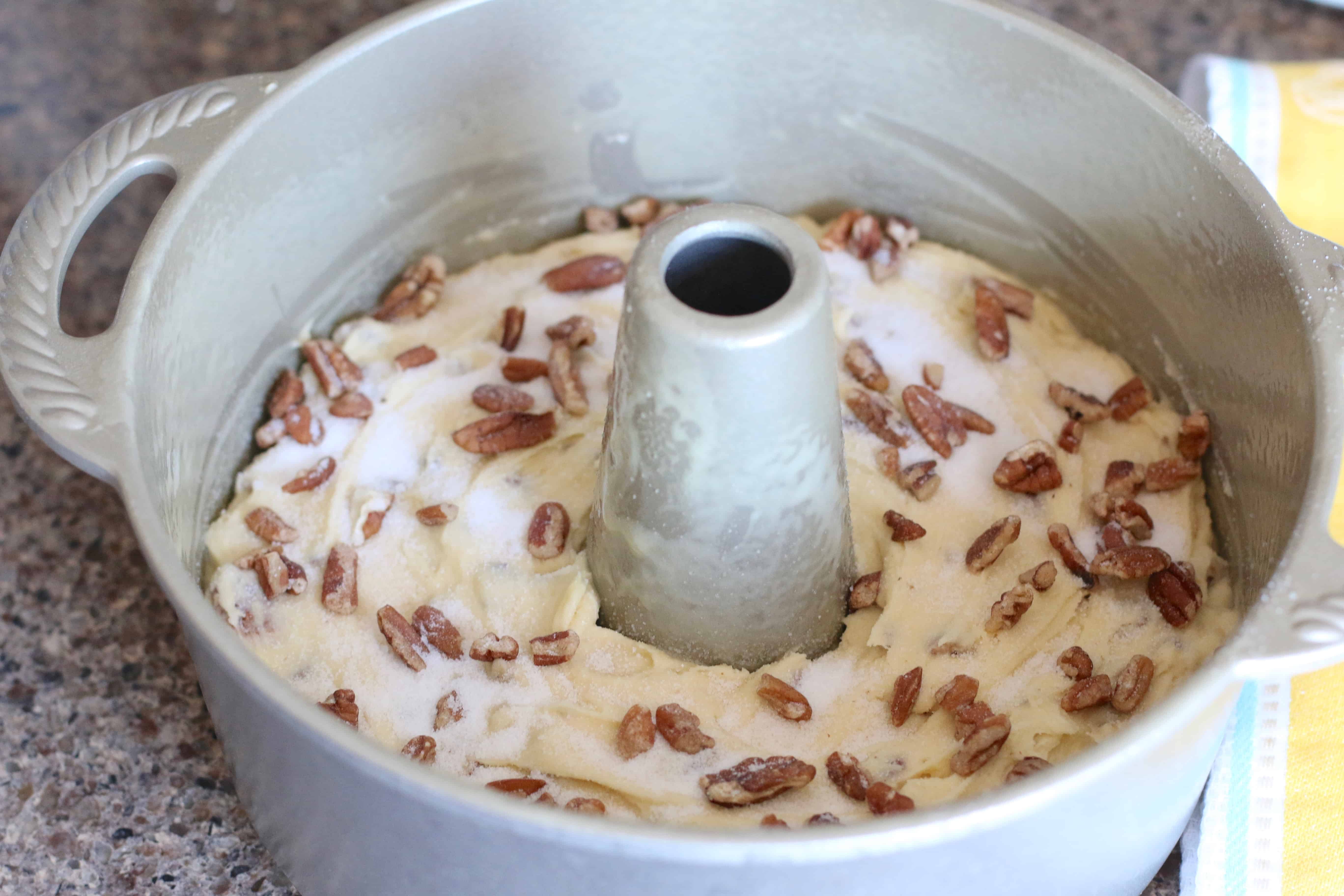 homemade pecan pound cake batter in a bundt pan sprinkled with pecans.