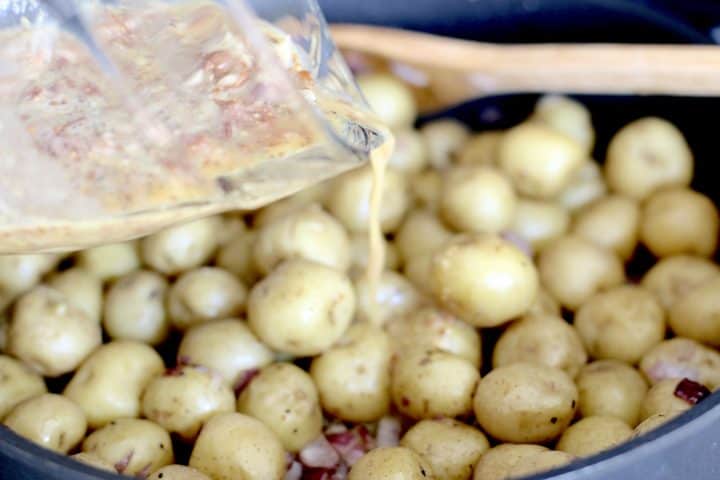 vinaigrette being poured into skillet with baby potatoes.