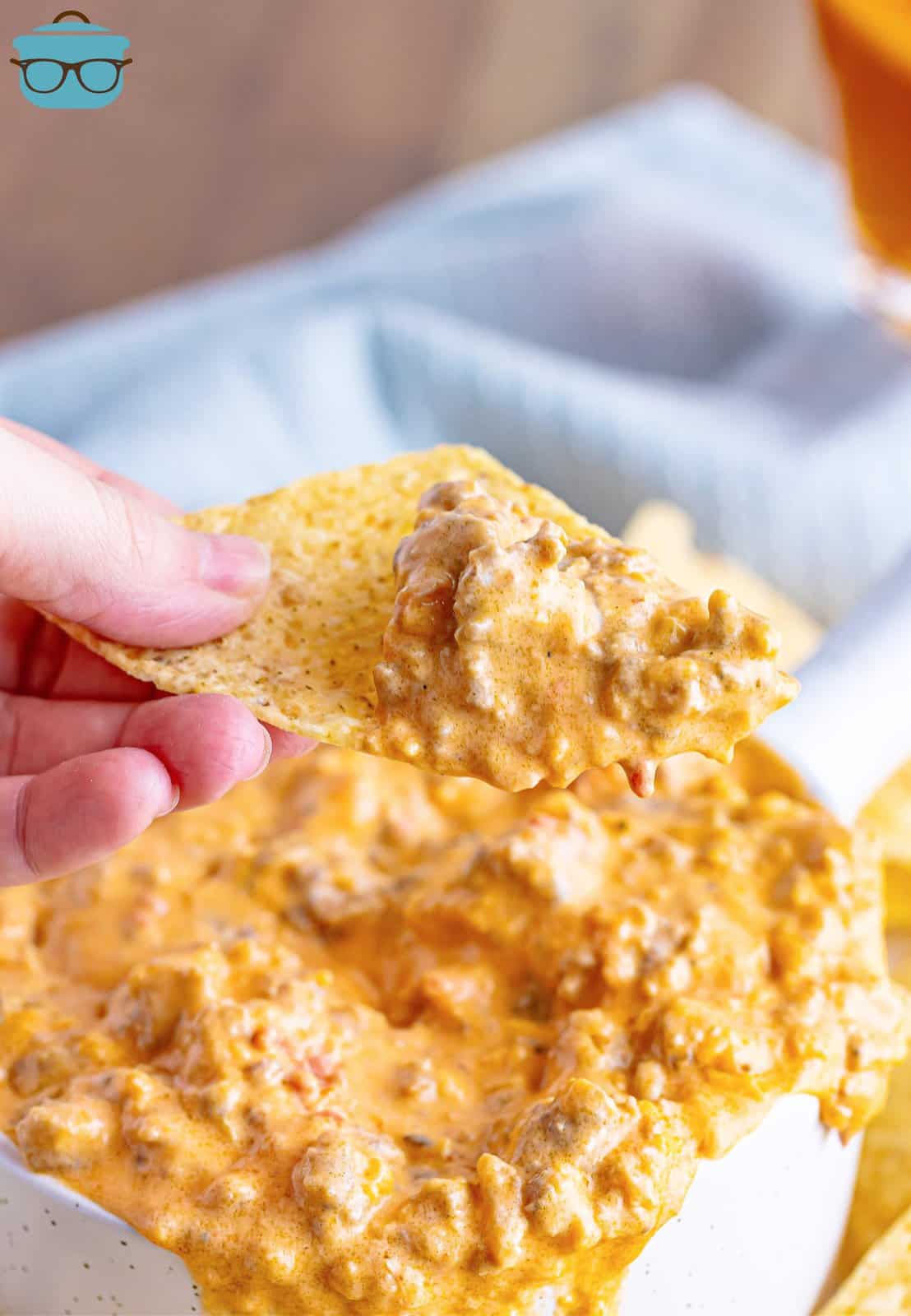 a hand holding up a tortilla chip with some pimento cheese sausage dip on the end of it. 