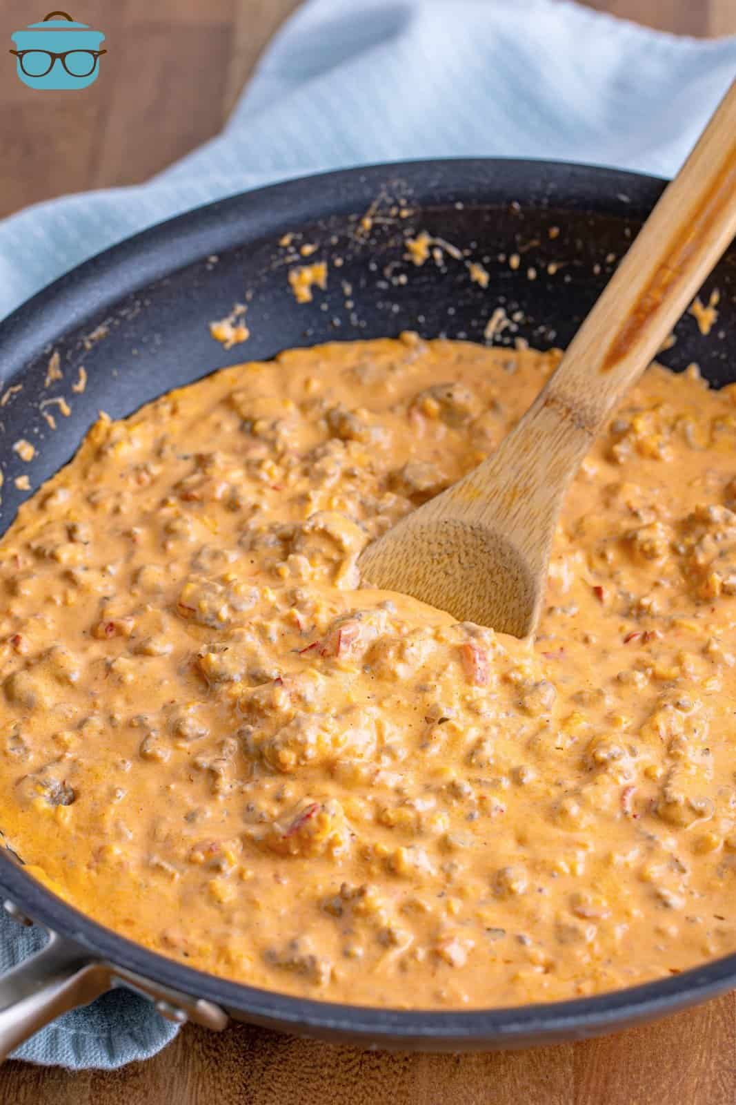 pimento cheese sauce dip shown in a large skillet with a wooden spoon. 