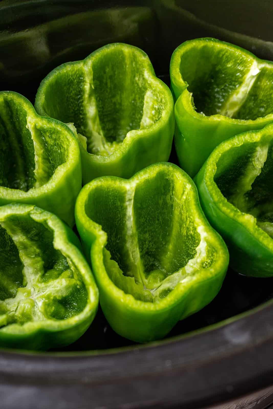 six green peppers shown in an oval black slow cooker. 
