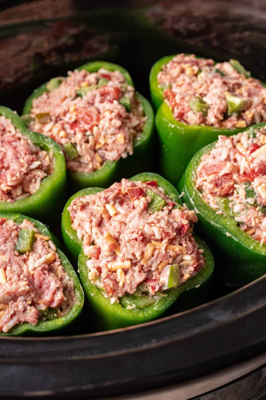 uncooked meat mixture shown stuffed into each green pepper in the slow cooker. 