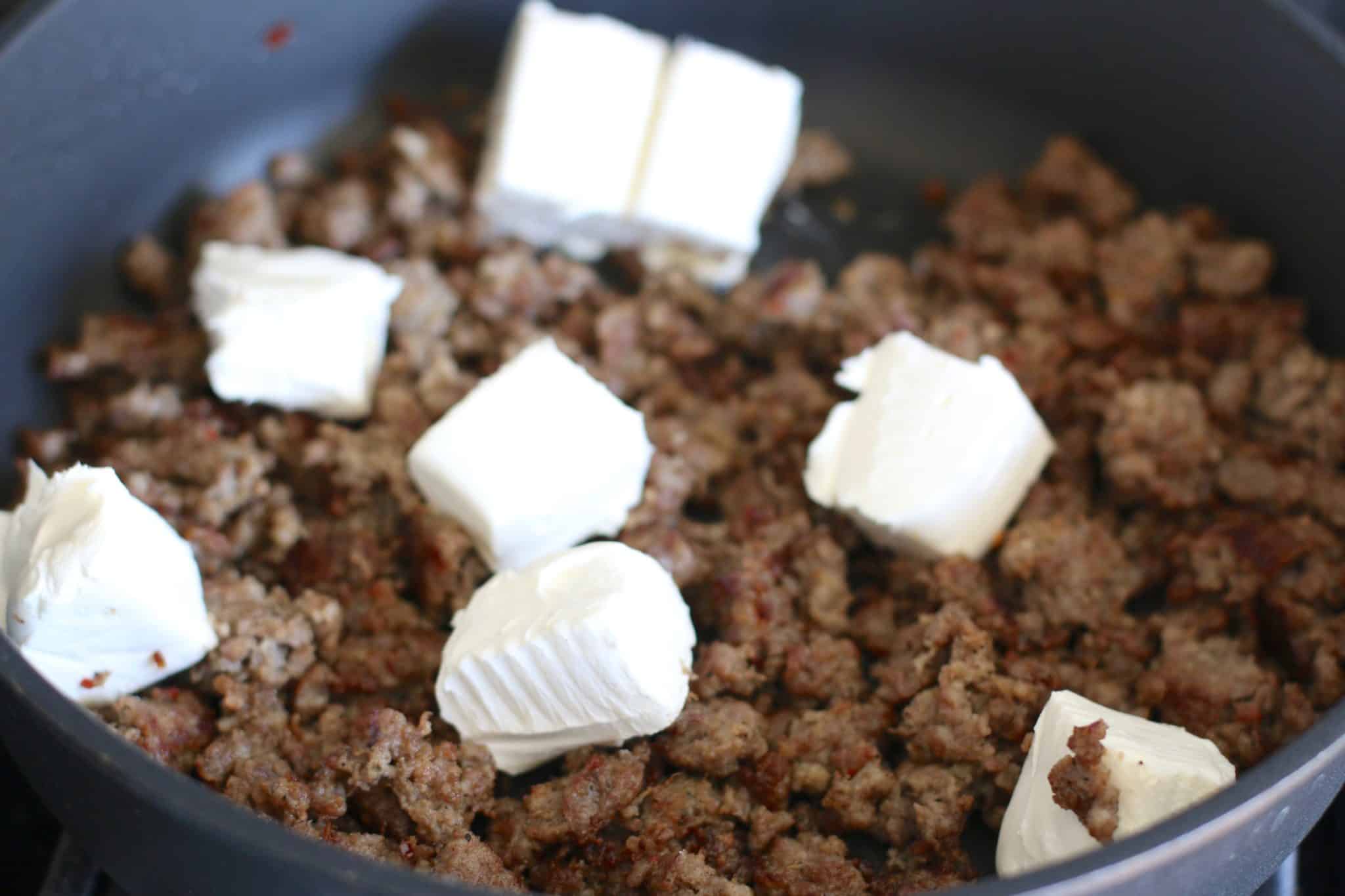 cubed cream cheese and cooked sausage in skillet.