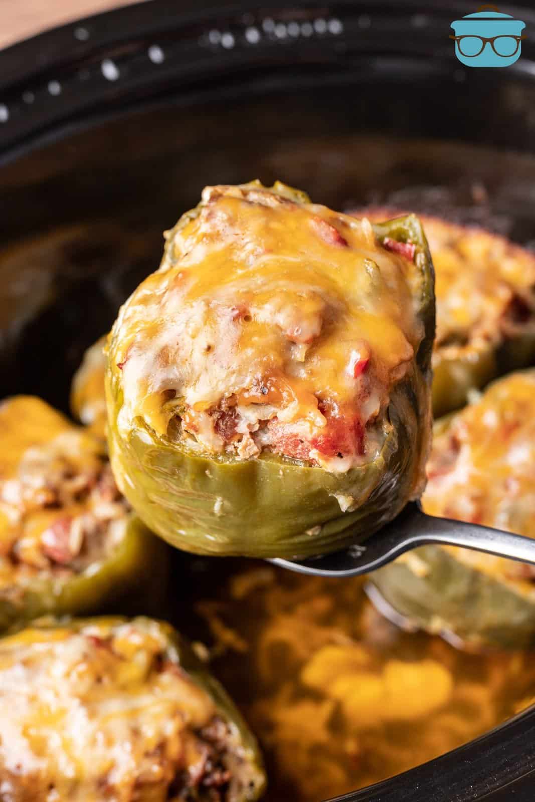 a spoon holding up one of the cooked stuffed peppers over the slow cooker. 