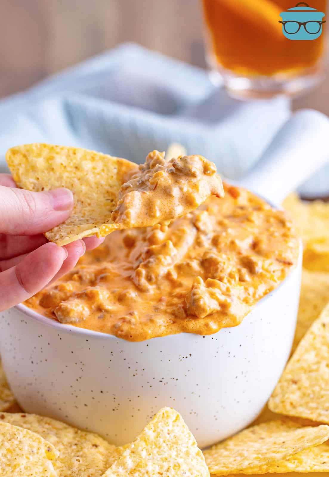 white bowl of pimento cheese sausage dip with a tortilla chip that has been dipped in and scooped out some of the dip. 
