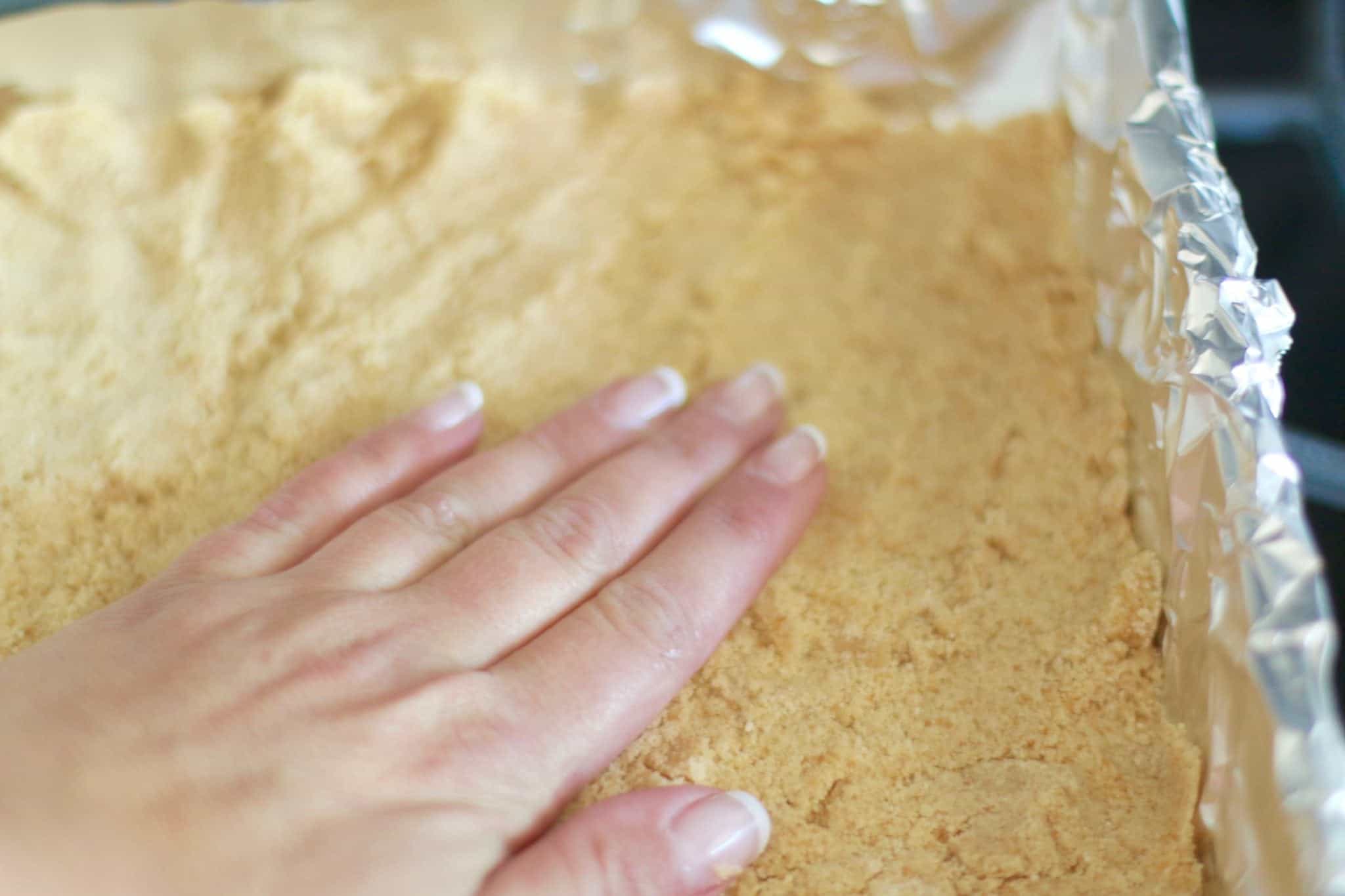 pressing crumbs into aluminum foil lined square baking pan.