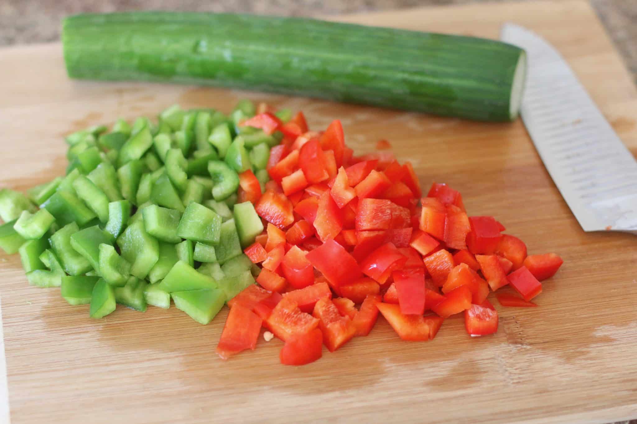diced cucumbers, green peppers, red pepper on wooden cutting board