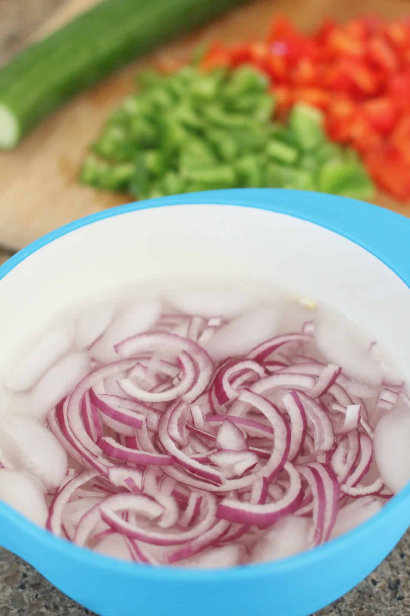 sliced red onions soaking in a bowl of ice water