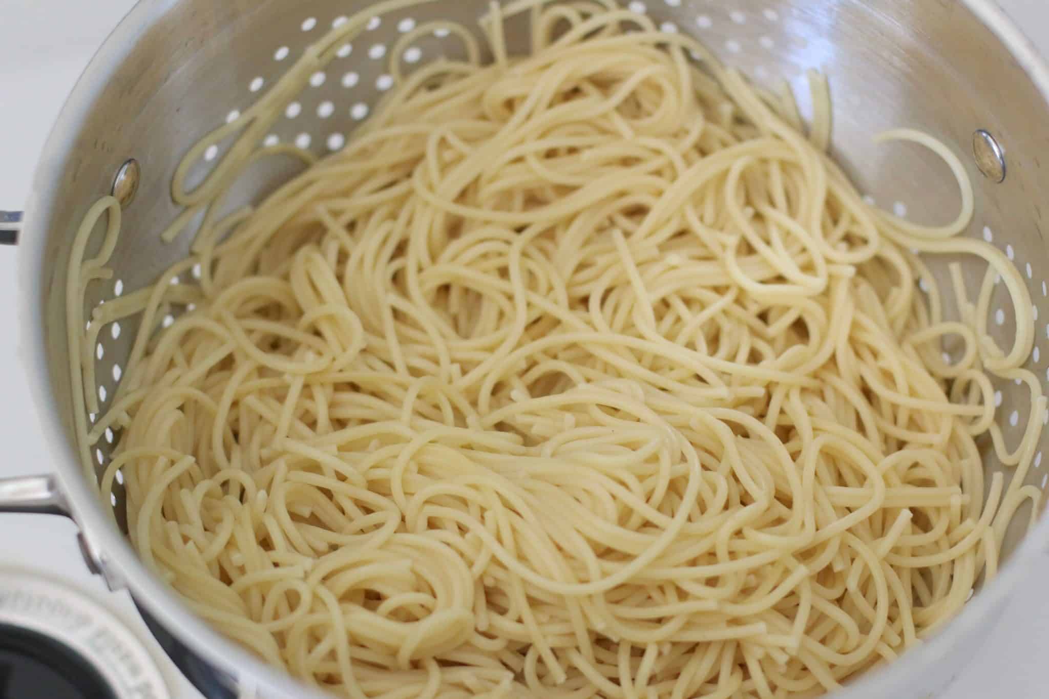 cooked spaghetti noodles in metal strainer.