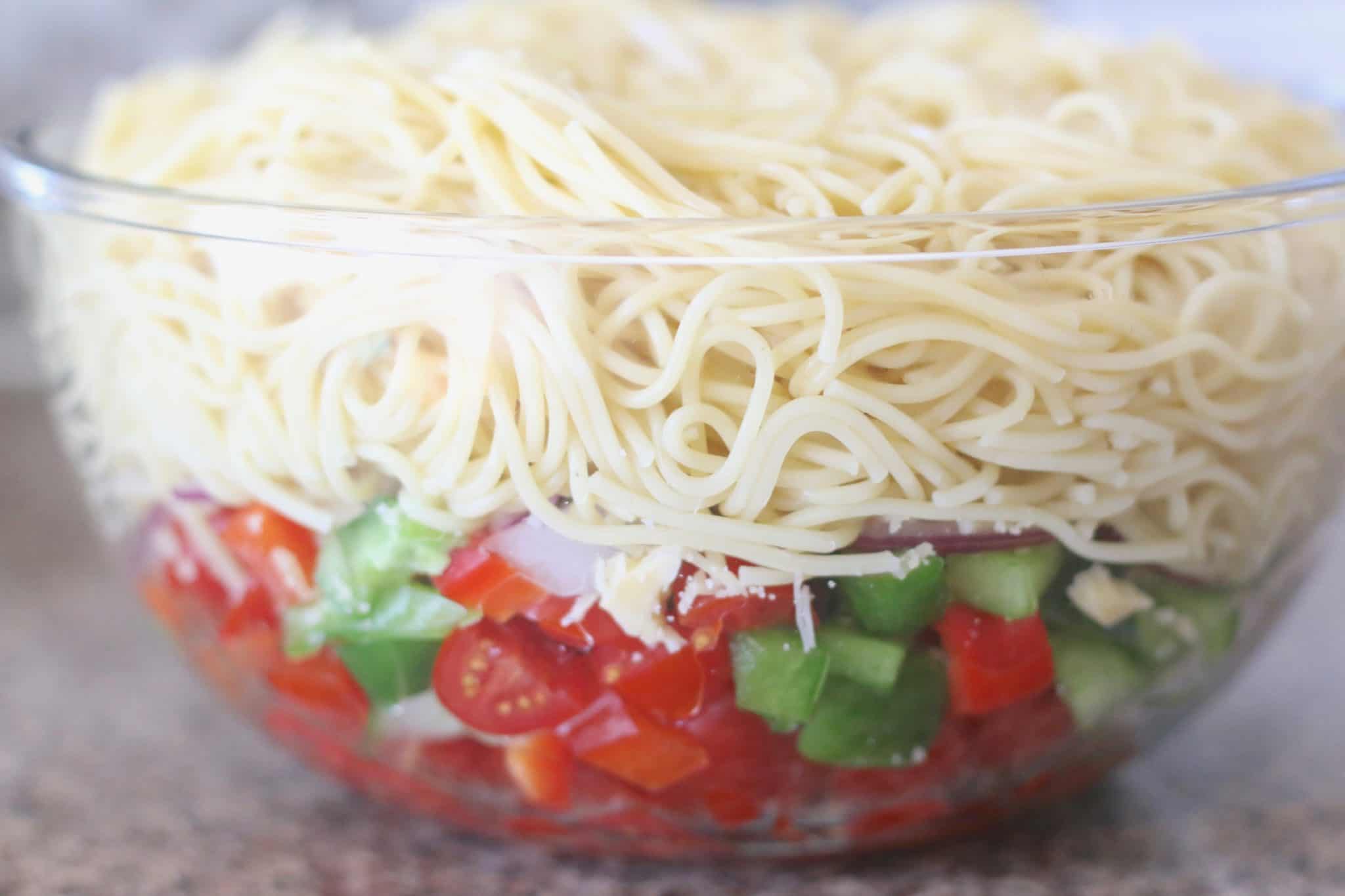 cooked spaghetti noodles, grape tomatoes, peppers, onions in a clear bowl