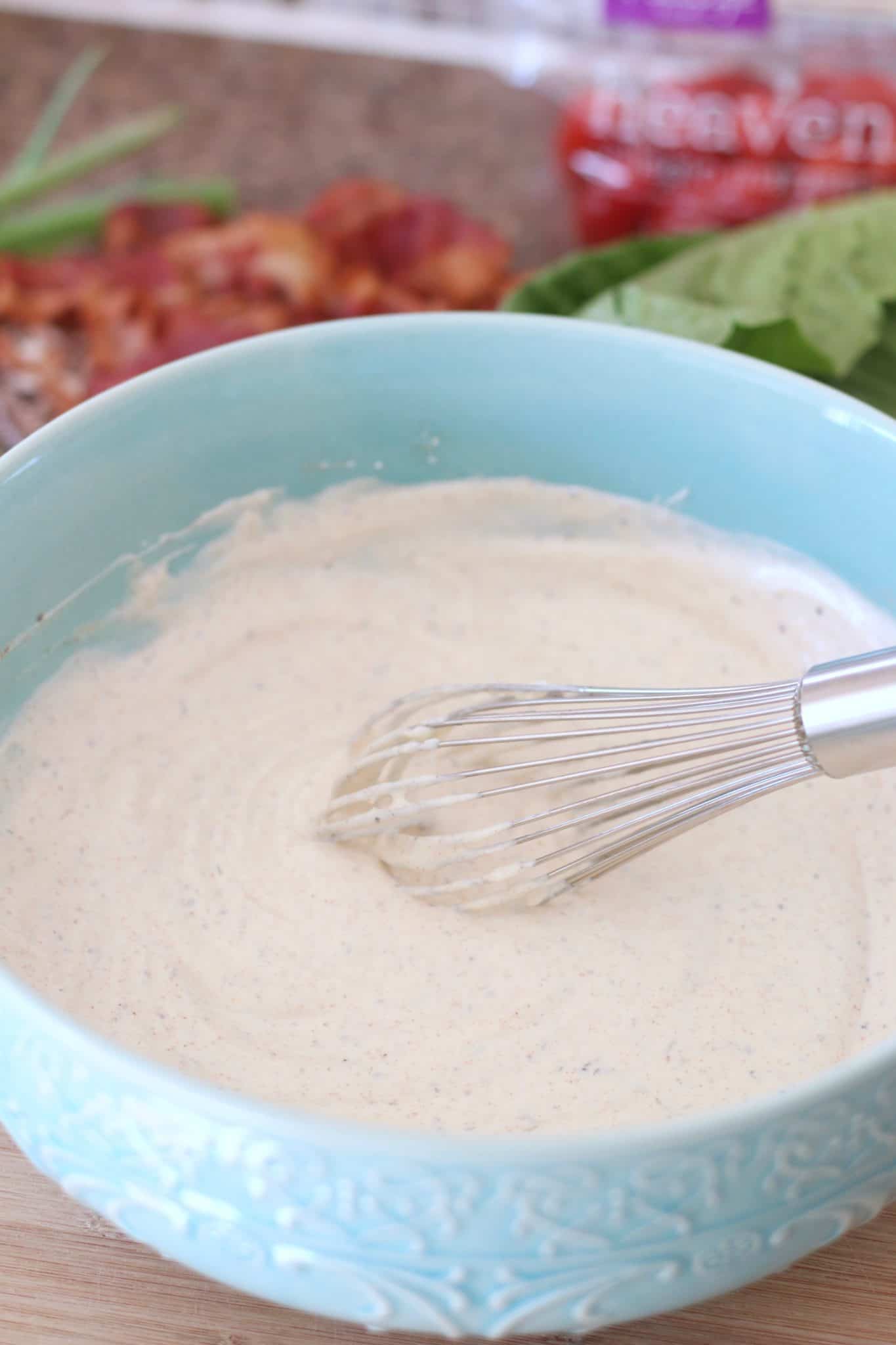 sour cream, mayonnaise, paprika, onion powder, garlic powder dressing whisk in a blue bowl.
